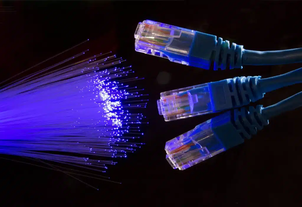 Fibra ótica brilhando em azul e roxo, com três cabos ethernet ao lado.